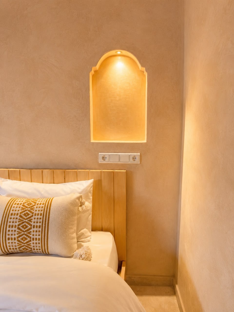 Lit arched niche above a bed in warm plaster