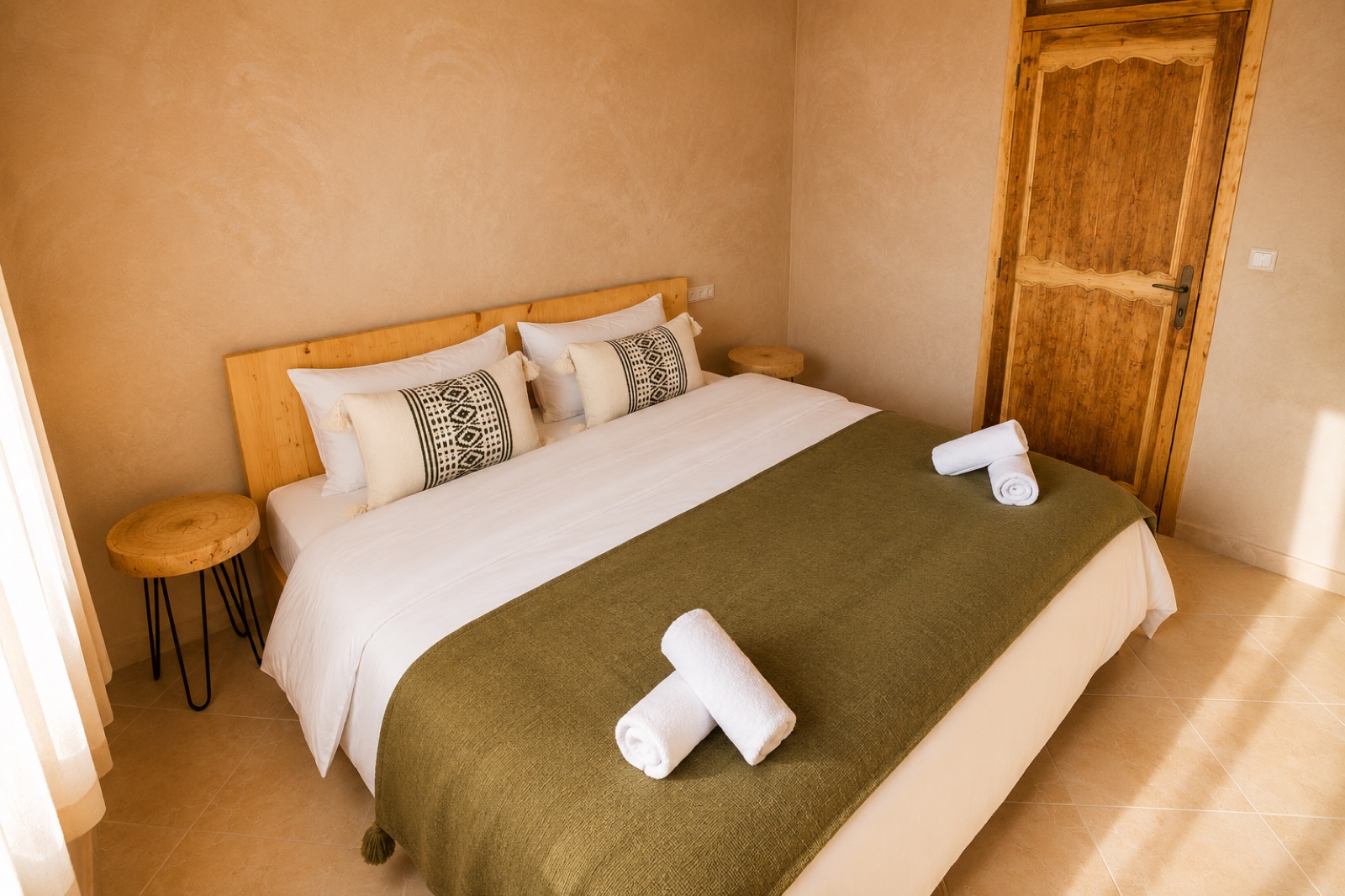 Double room with a green throw, white linen and a carved wooden door